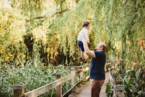 A father lifts his little boy above his as they stand on a boardwalk