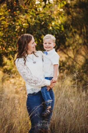 A mother holds her son in a long grass field at sunset