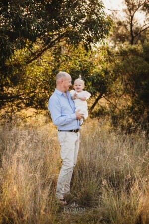 A dad holds his baby girl in a long grass field at sunset