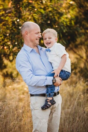 A dad holds his son in a long grass field at sunset