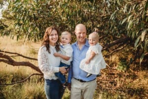A family stand huddled together in front of a tree