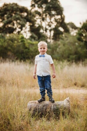A little boy stands on a log in the middle of a grass field