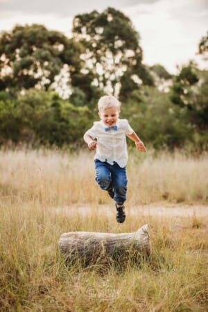 A little boy jumps off a log into long grass