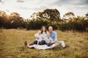 A family sit together on a rug in a grass field at sunset