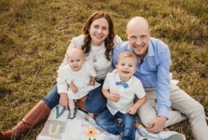 A family sit together on a bright colourful rug in a field