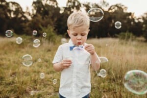 A little boy blowing bubbles in a grassy field at sunset