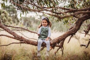 A little girl sits in a low tree branch at sunset
