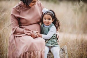 A little girl sits with her hand on her mum's pregnant belly