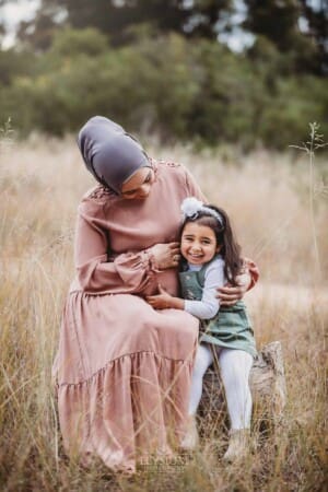 A mother sits on a log cuddling her little girl