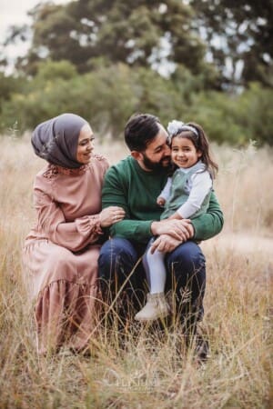 Parents sit on a log and cuddle their little girl