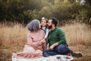 Parents sit on a rug and cuddle their little girl