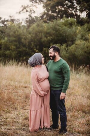 A man hugs his pregnant wife, she has a pink maternity gown