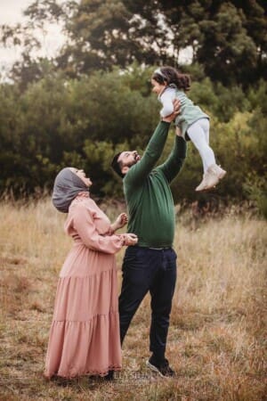 Parents lift their little girl into the air as they all laugh