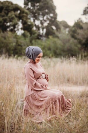 A pregnant mother wearing a pink maternity gown in long grass