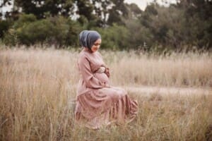 A pregnant mother wearing a pink maternity gown in long grass