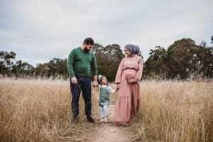 Parents hold their little girl's hands as they walk in long grass