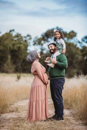 Parents stand in long grass, a little girl sits on her dad's shoulders