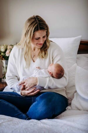 A mother sits on a bed holding her newborn in her arms