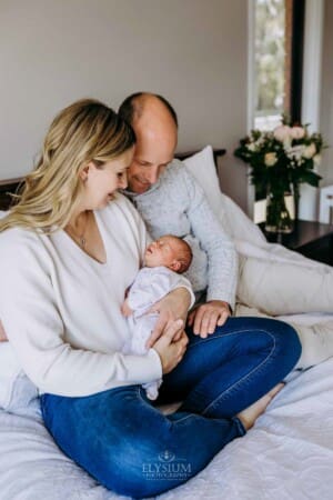 Parents sit on a bed holding their newborn baby girl