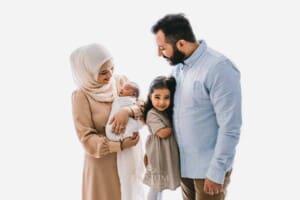A family stand against a bright window holding their newborn