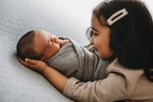 A little girl holds her newborn brother in her arms