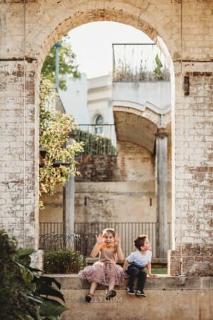 Paddington Gardens, kids sit beneath a stone arch pulling faces