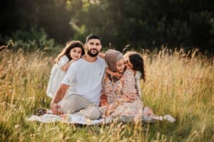 Parents sit in a grassy field as their little girls cuddle them both