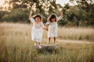 2 Little girls hold hands and jump off a log into long grass