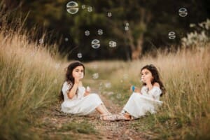 2 little girls sit on a dirt path and blow bubbles