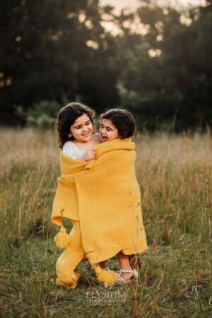 2 little girls wrapped in a yellow blanket giggle in a grass field