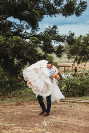 Gledswood Wedding - a groom carries his bride over his shoulder on a dirt driveway at the venue