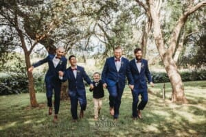 Gledswood Wedding - groomsmen run holding hands in the gardens at the venue