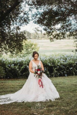 Gledswood Wedding - a bride stands holding her bouquet in the gardens at the venue