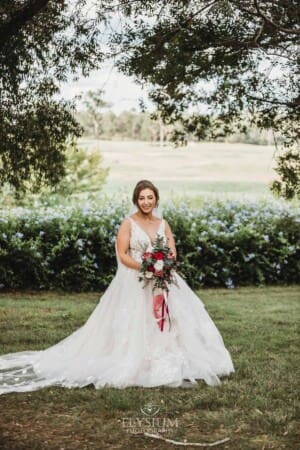 Gledswood Wedding - a bride stands holding her bouquet in the gardens at the venue