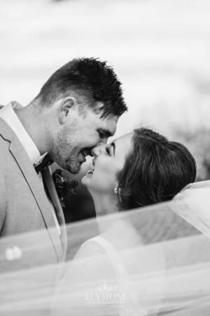 Gledswood Wedding - a groom kisses his bride standing wrapped in the bride's veil