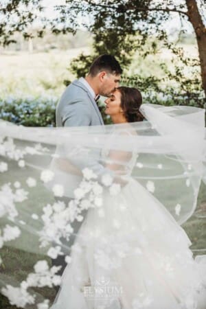 Gledswood Wedding - a groom kisses his bride standing wrapped in the bride's veil