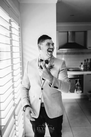 Gledswood Wedding - Groom applies cologne next to a bright window during morning prep