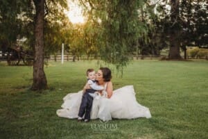 Gledswood Wedding - a bride kisses her little boy as they sit under a pepper tree at sunset