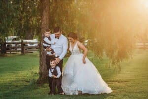 Gledswood Wedding - a bride and groom stand with their children under a pepper tree at sunset