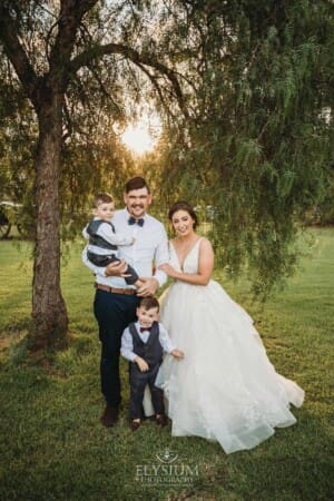 Gledswood Wedding - a bride and groom stand with their children under a pepper tree at sunset