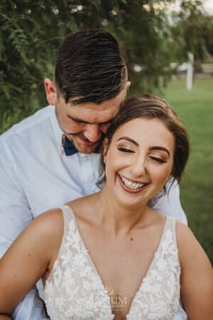 Gledswood Wedding - a groom cuddles his bride as they stand under a pepper tree at sunset