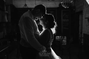 Gledswood Wedding - Newlyweds stand in a dark room with a bright light behind them