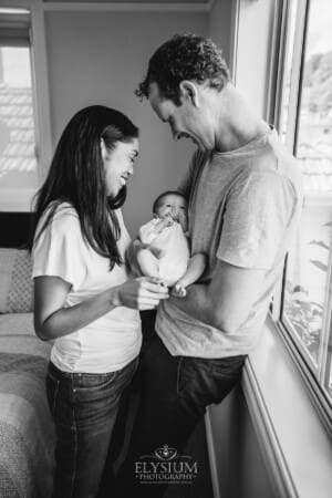 Parents hold their newborn baby between them and smile