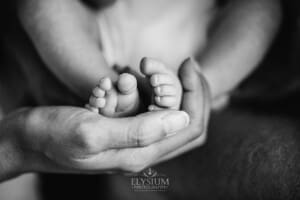 A mother's hands gently cup her newborn baby's tiny feet