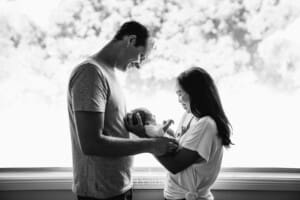 Parents hold their newborn baby between them and smile