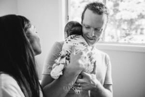 Parents hold their newborn baby between them and smile