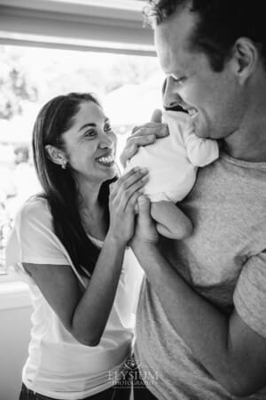 Parents hold their newborn baby between them and smile