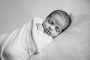 A tiny newborn lays on a white blanket in a white wrap