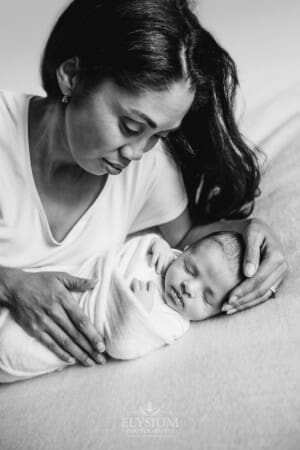 A mother lays beside her newborn baby girl wrapped in a white blanket