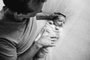 A father lays beside his newborn baby girl wrapped in a white blanket